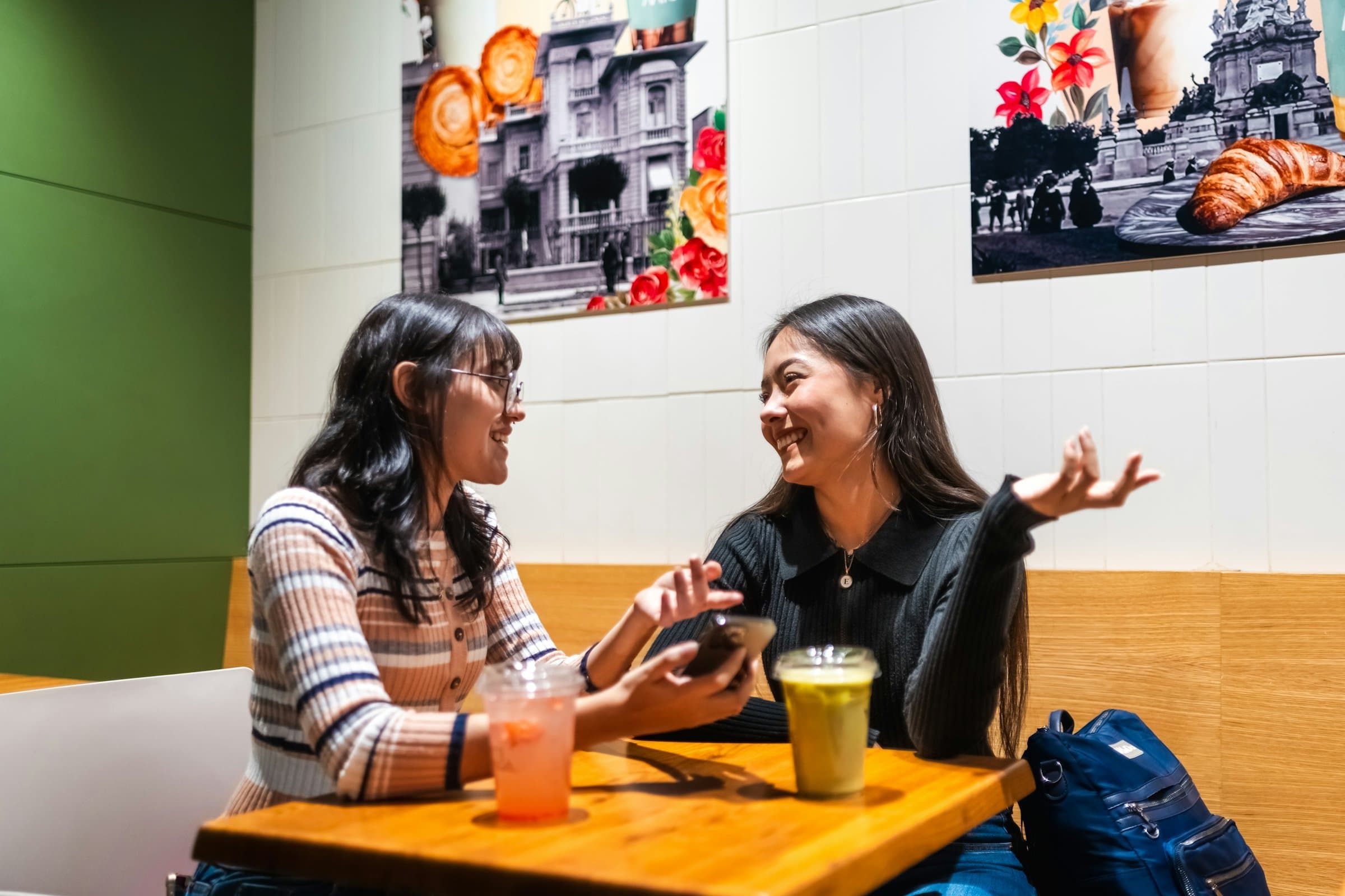 Two young women chatting animatedly over juices at a bright café table