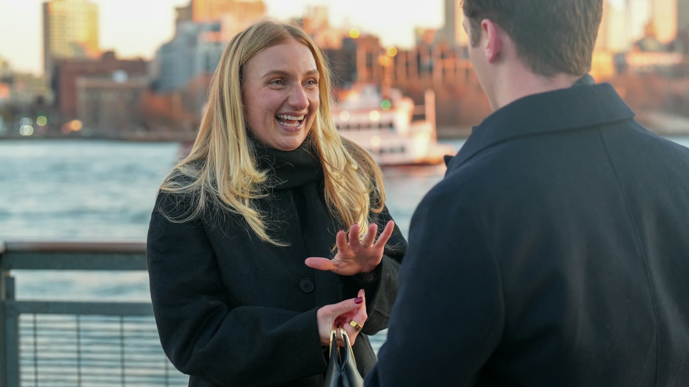 A woman laughing mid-conversation with a man by the water at golden hour